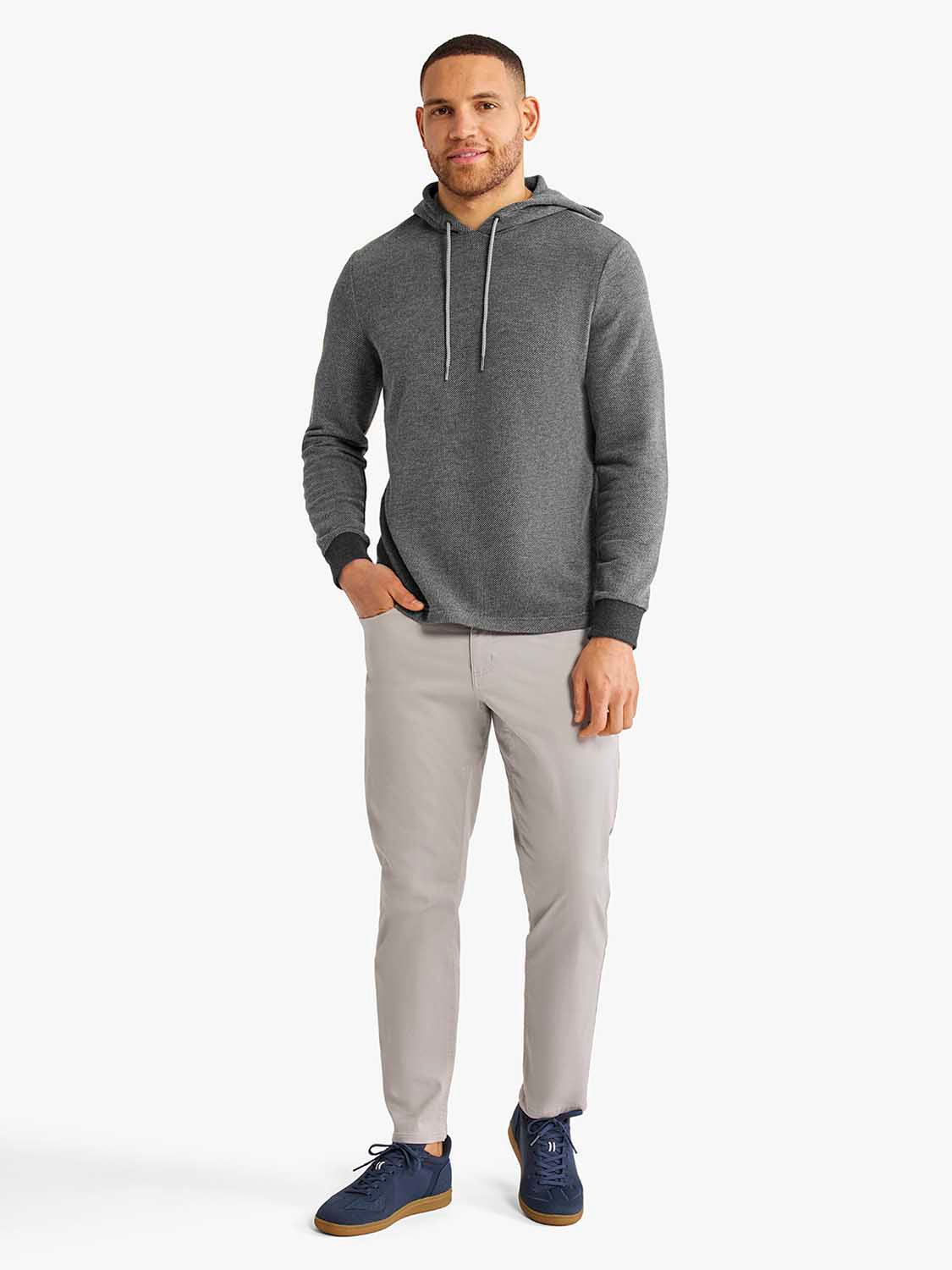 Man wearing a charcoal gray hoodie with drawstring and light gray pants standing against white background.