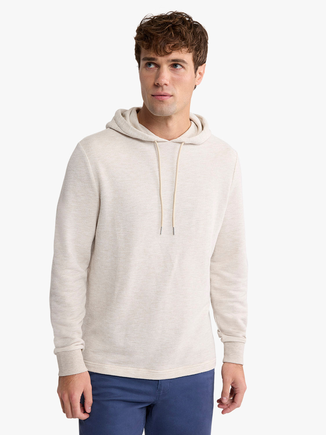 Man wearing a natural beige hoodie with drawstrings and navy pants against a white background.
