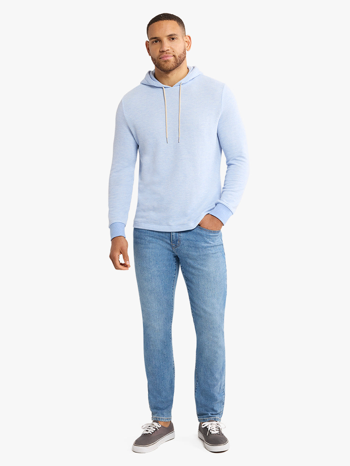 Man wearing a light blue hoodie with drawstrings and blue jeans standing against a white background.