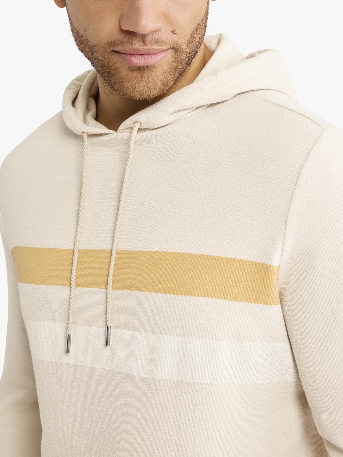 Man wearing a cream terry hoodie with a gold horizontal stripe across the chest.