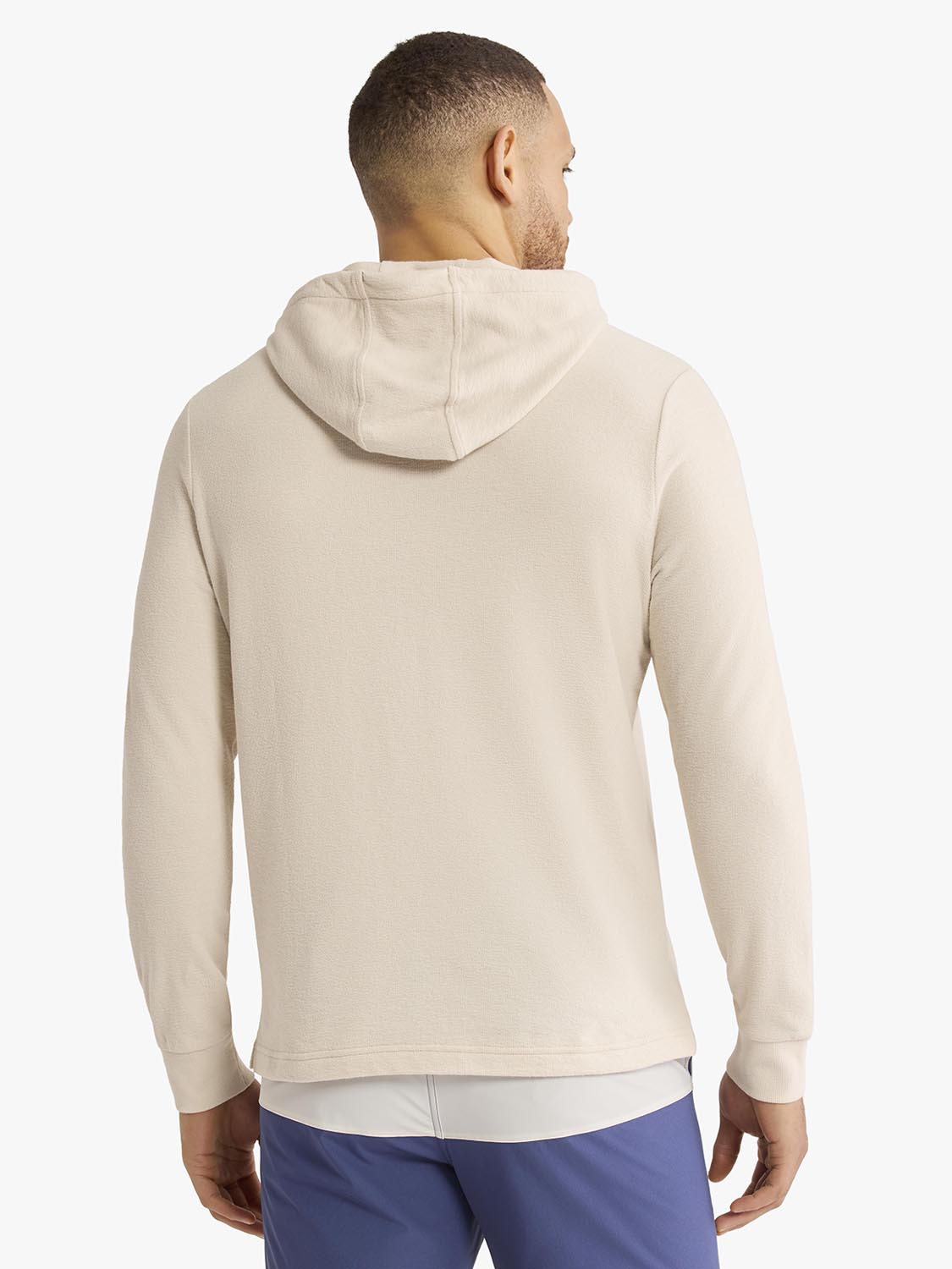 Man wearing a cream-colored terry hoodie with a drawstring hood, shown from the back.