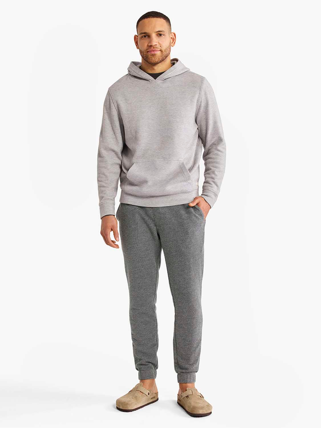 Man wearing a light gray hoodie and charcoal jogger sweatpants with cuffed ankles and side pockets.