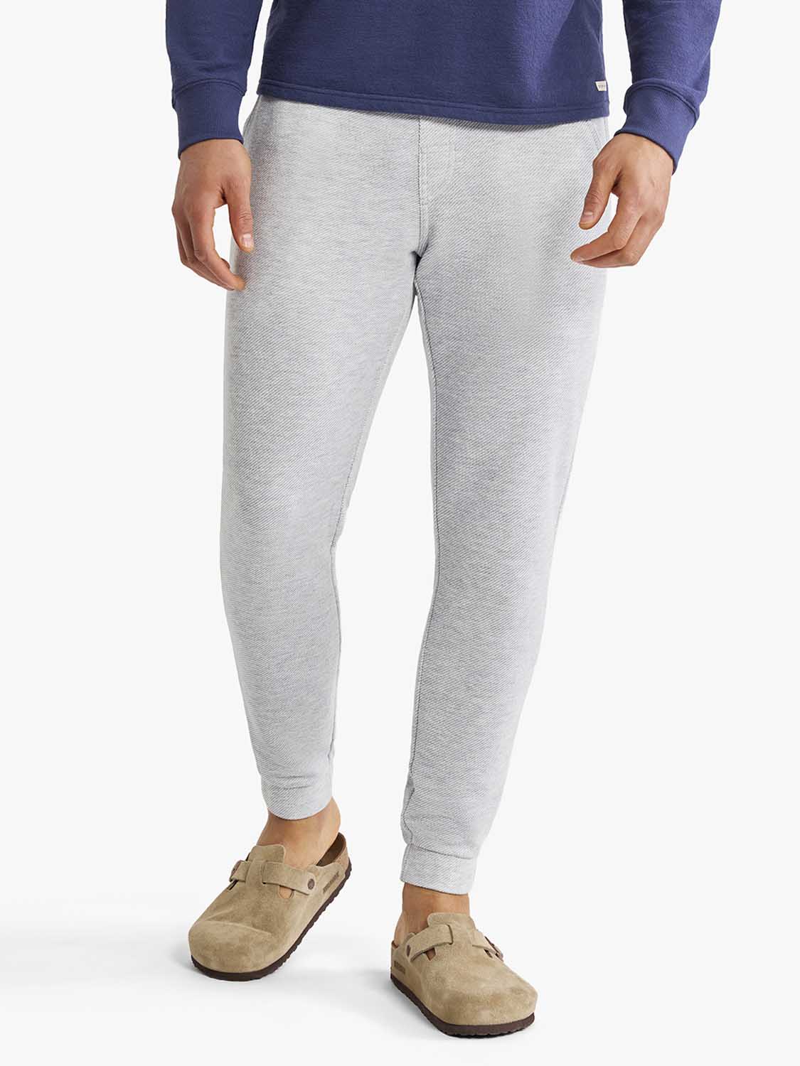 Man wearing heather grey sweatpants with a navy blue sweatshirt and tan suede clogs.