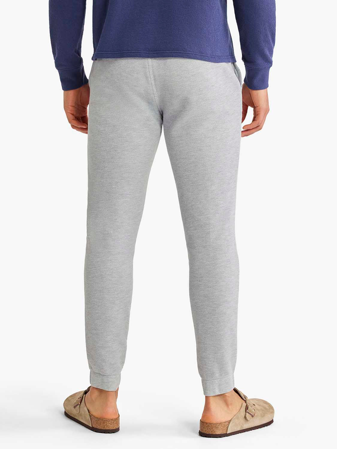 Man wearing heather grey sweatpants with an elastic waistband and cuffed ankles from behind.