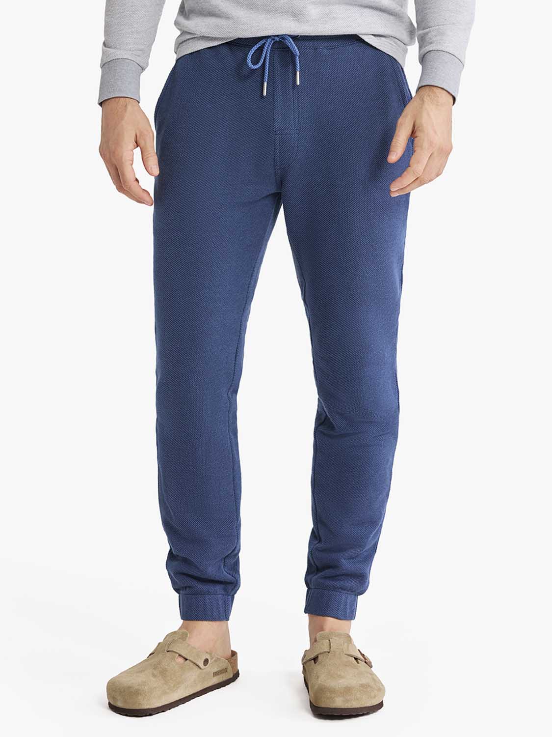 Man wearing navy blue sweatpants with drawstring waist and ribbed cuffs paired with gray sweatshirt.