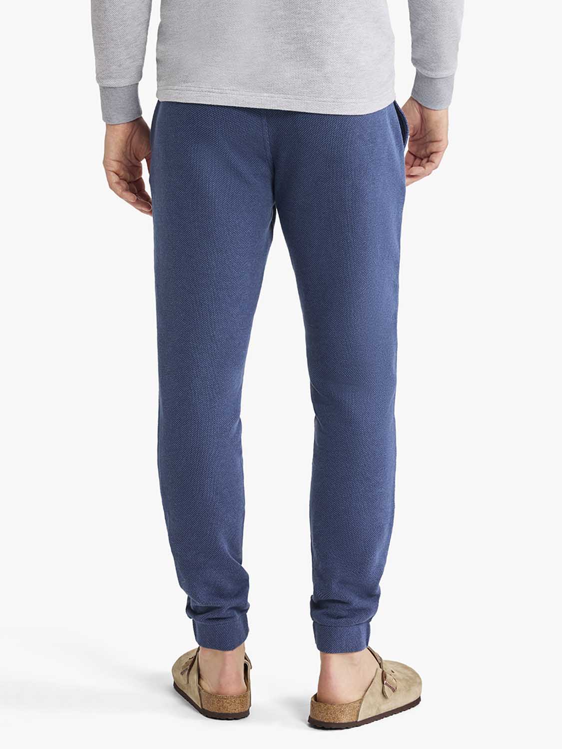 Navy sweatpants with ribbed cuffs worn with a gray sweatshirt and tan slip-on shoes.