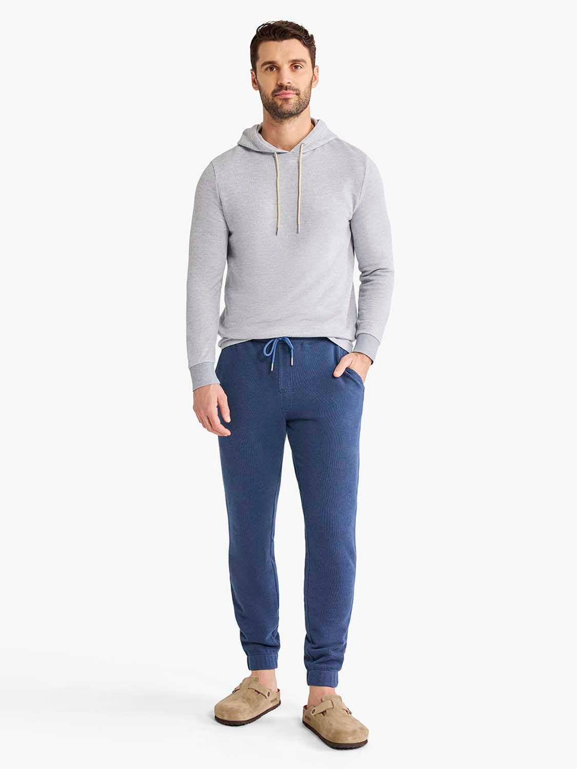 Man wearing gray hoodie and navy sweatpants with drawstring waist and cuffed ankles.
