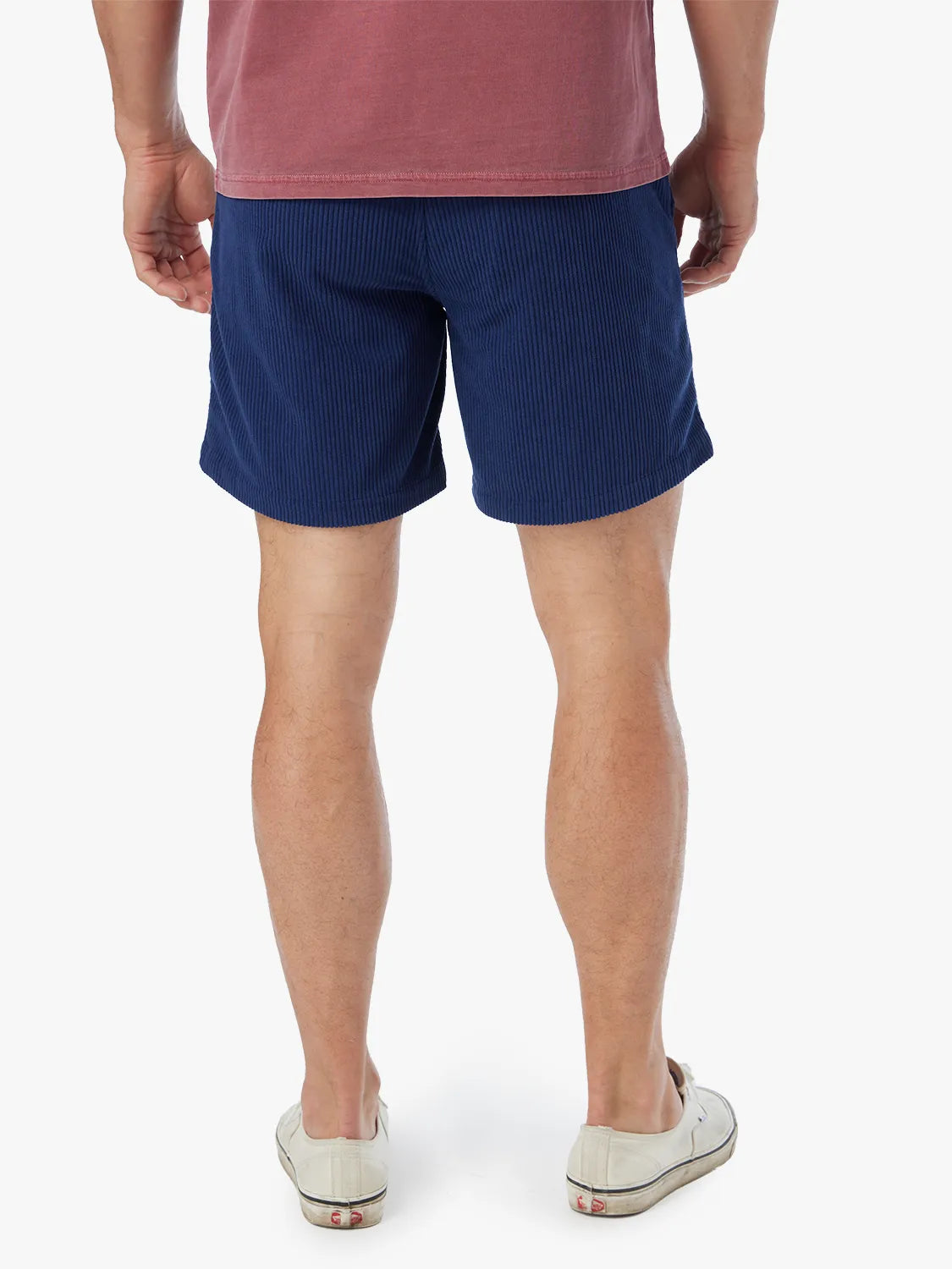 Man wearing navy corduroy shorts with visible vertical ribbed texture and white canvas sneakers.