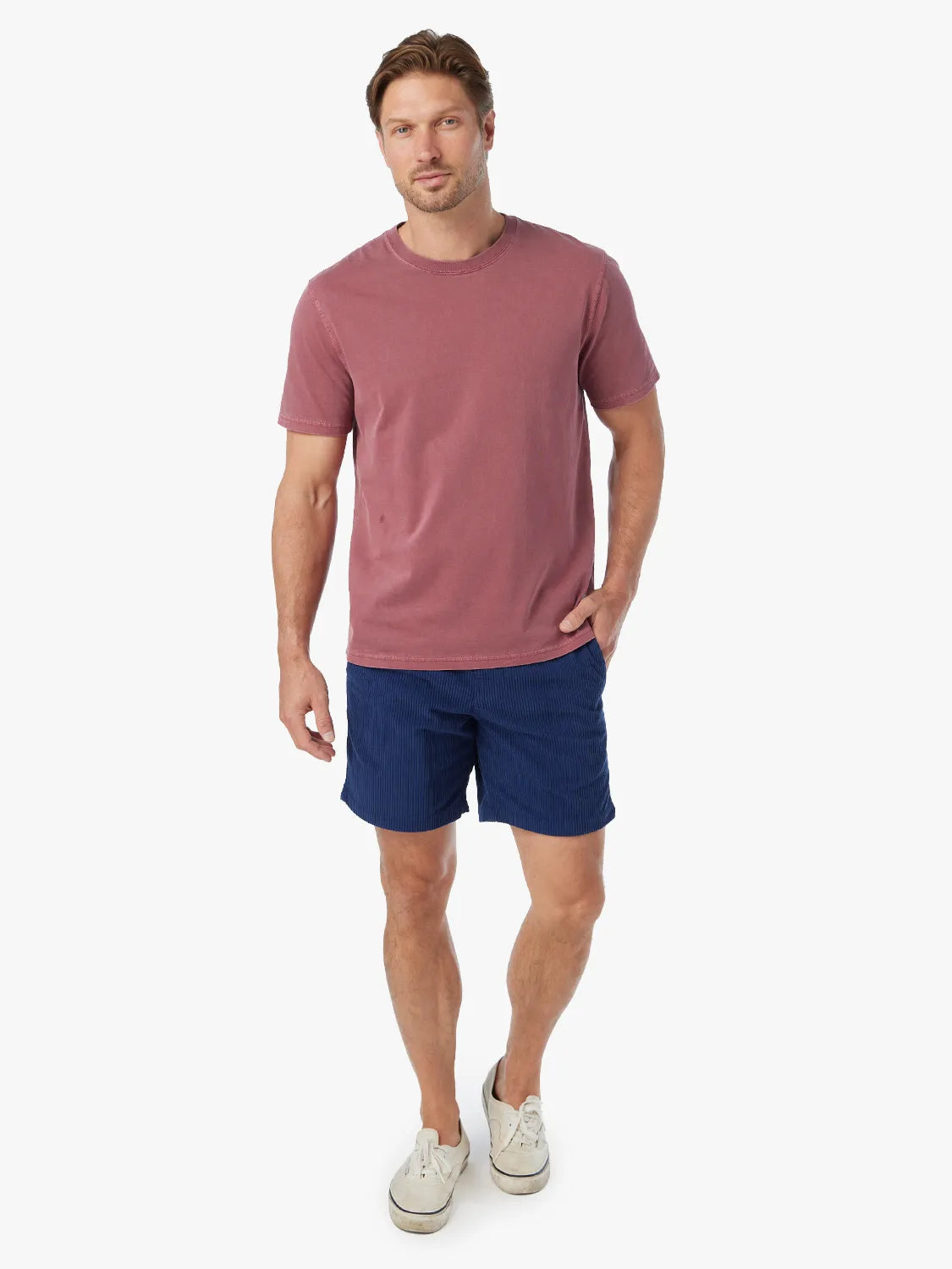Man wearing a mauve t-shirt and navy corduroy shorts with white sneakers.