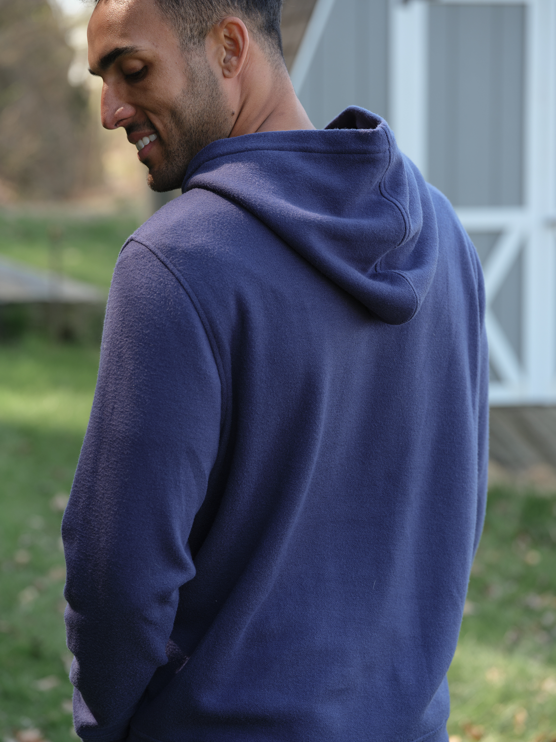 Man wearing a heather grey blanket hoodie with a large kangaroo pocket, shown from the back outdoors.