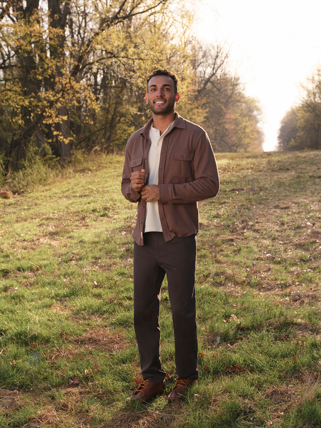 Man wearing an espresso brown flannel shirt over a white shirt standing outdoors on a dirt road.