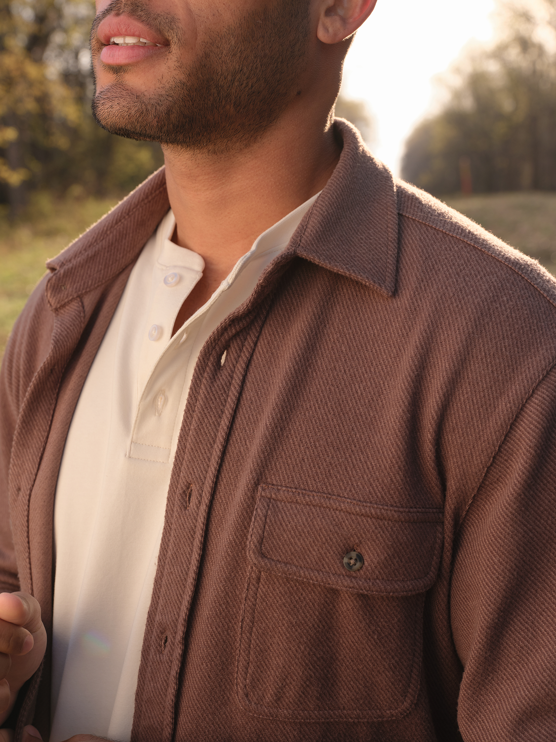 Man wearing a brown espresso twill flannel shirt with a white shirt underneath in an outdoor setting.