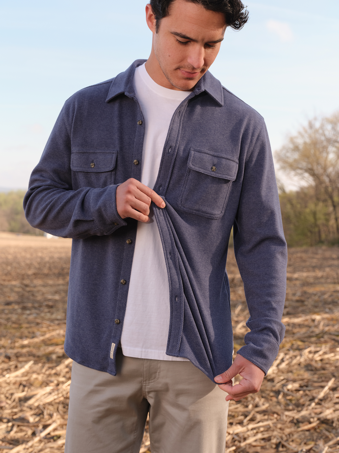Man wearing navy twill flannel shirt over white t-shirt with khaki pants in outdoor field.