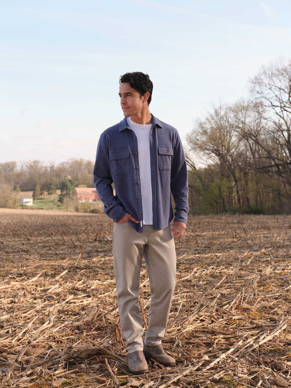 Man wearing a navy button-front flannel shirt over a white t-shirt and tan pants standing in a field.