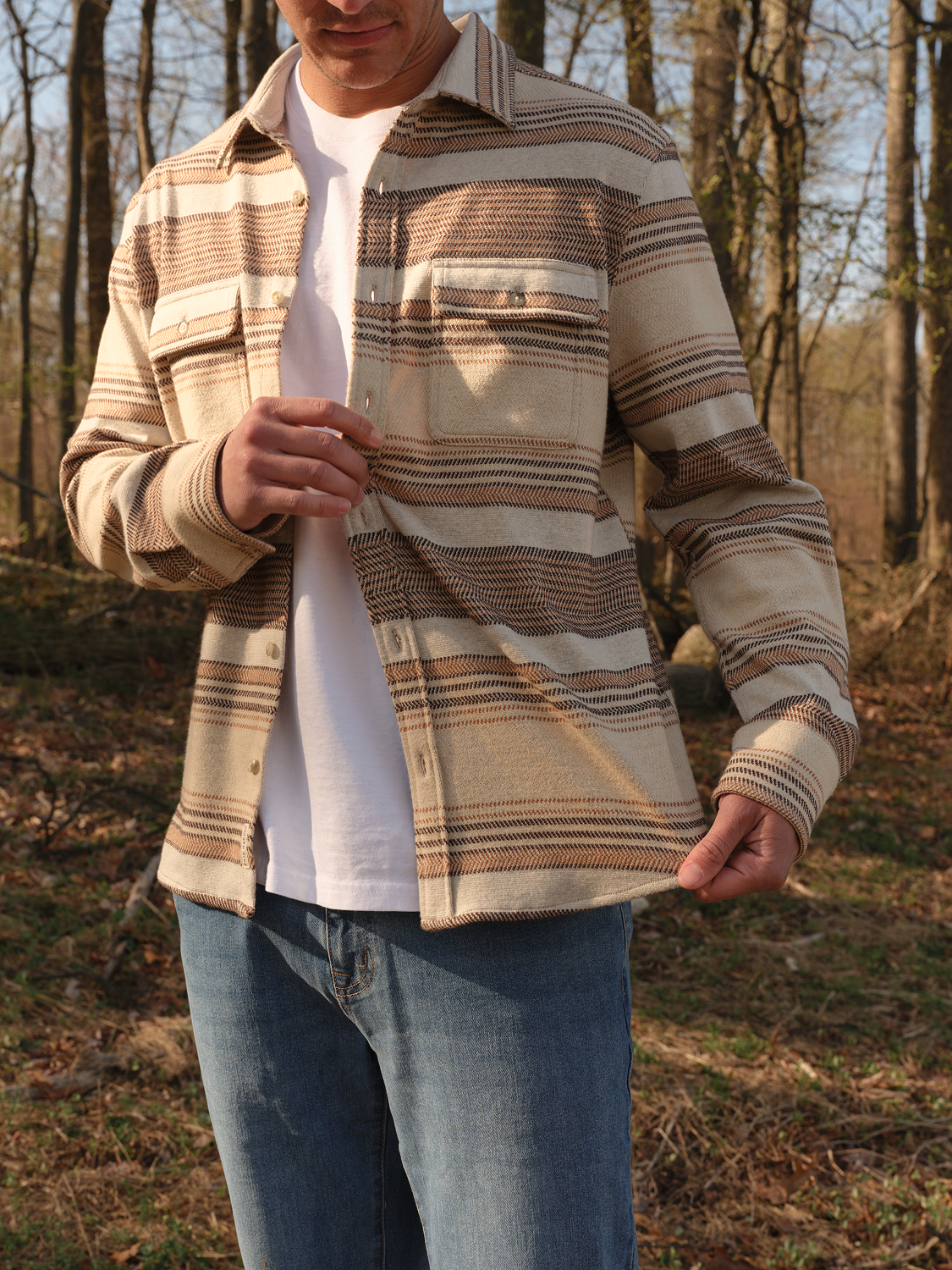 Man wearing a beige and tan striped flannel shirt over a white t-shirt with jeans.