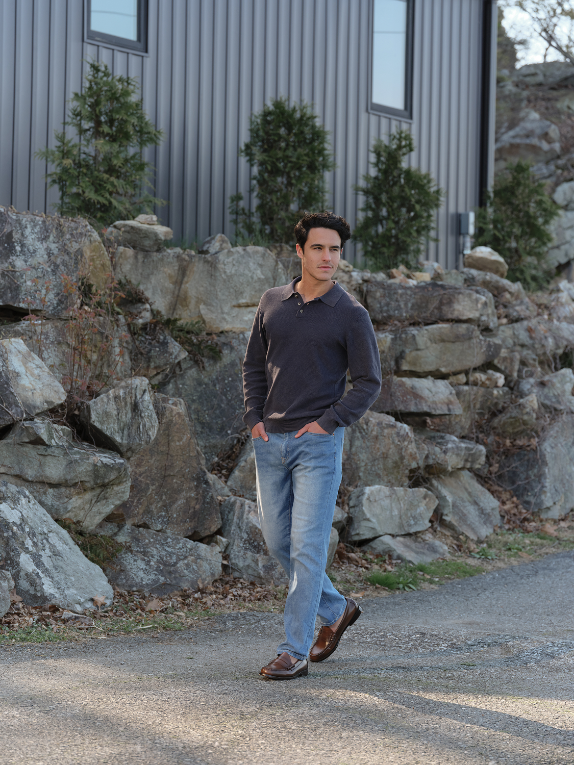 Man wearing a seastone long sleeve polo shirt and light blue jeans standing outdoors.