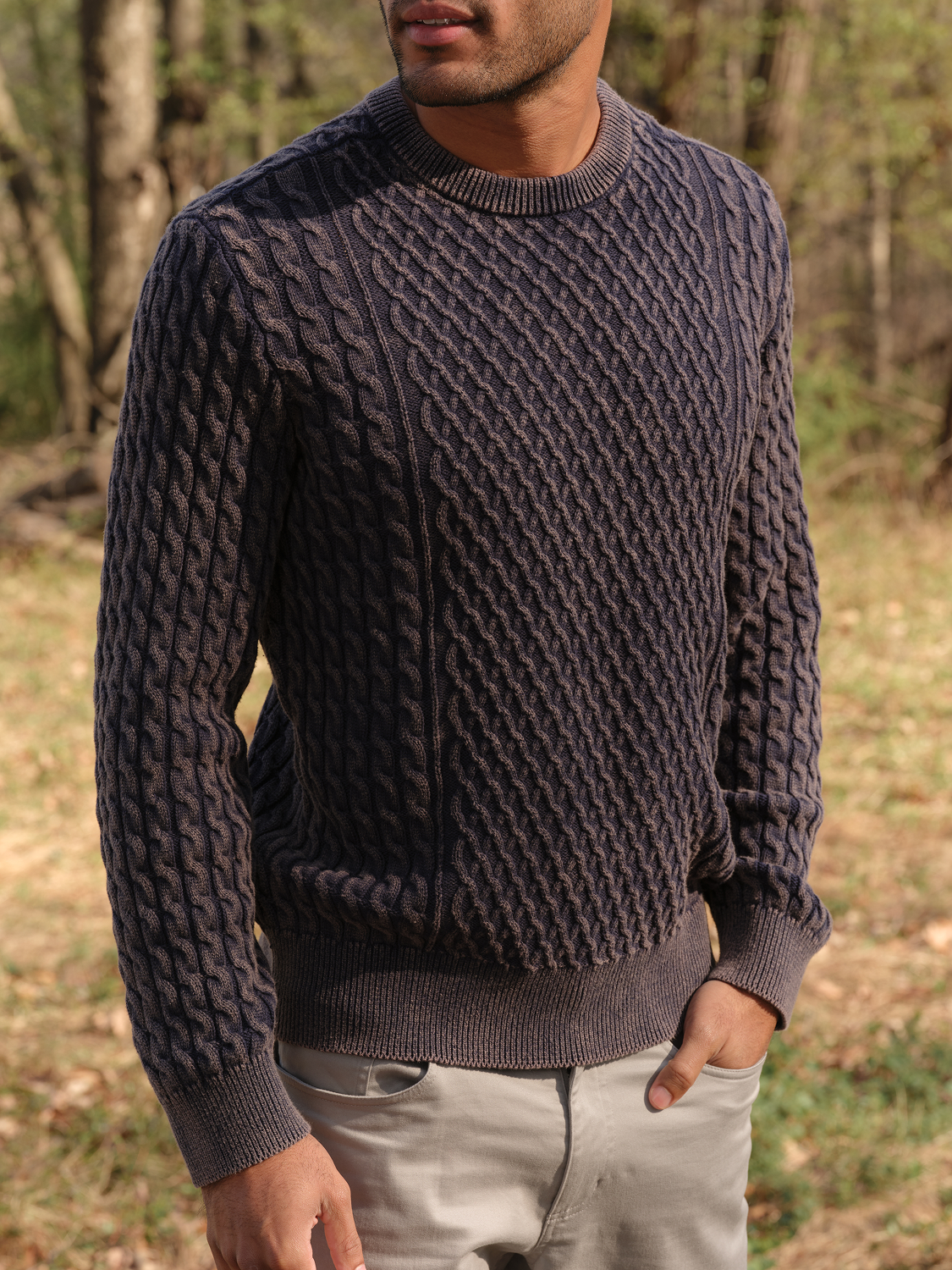 Man wearing a gray cable knit crewneck sweater with ribbed cuffs and hem.