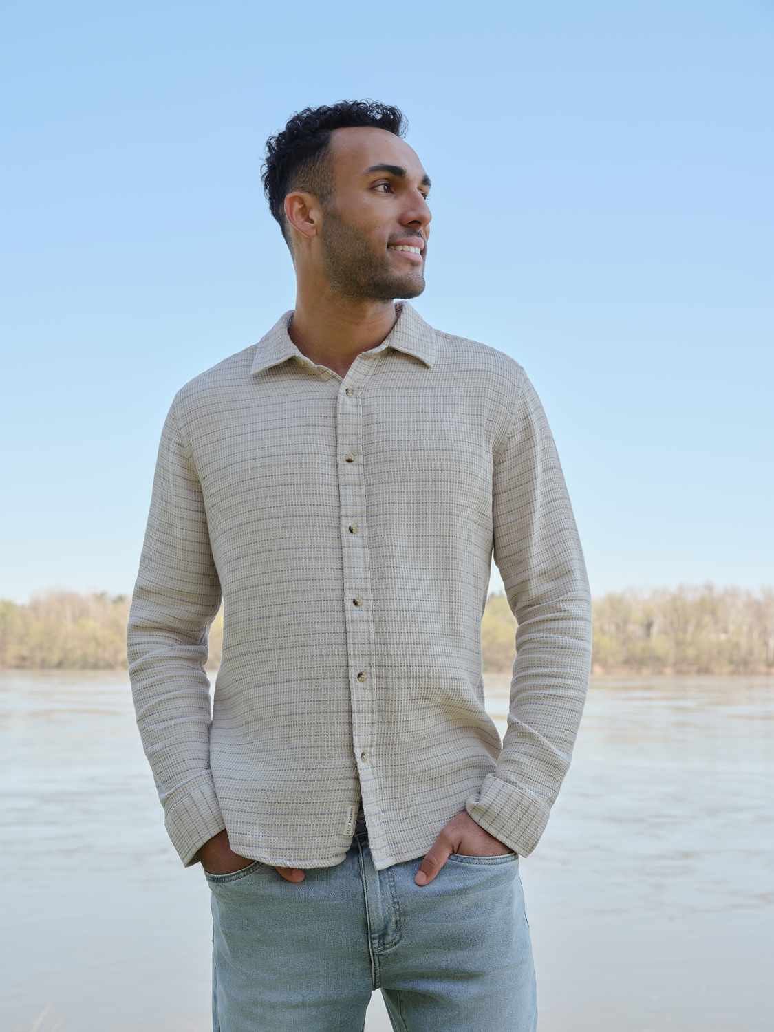 Man wearing a beige waffle striped long sleeve button up shirt over blue jeans.
