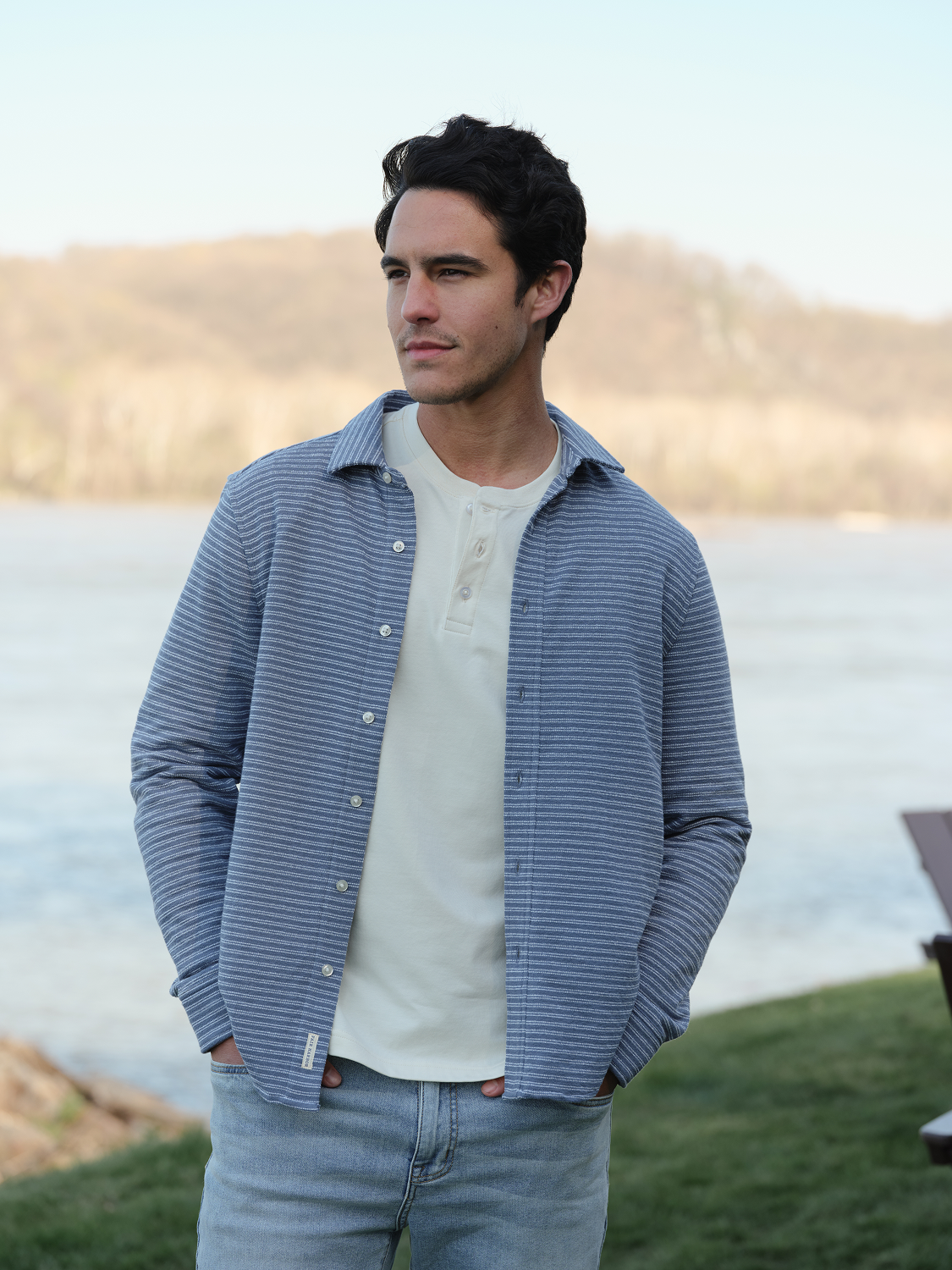 Man wearing a blue and white striped button-up shirt over a cream henley shirt.