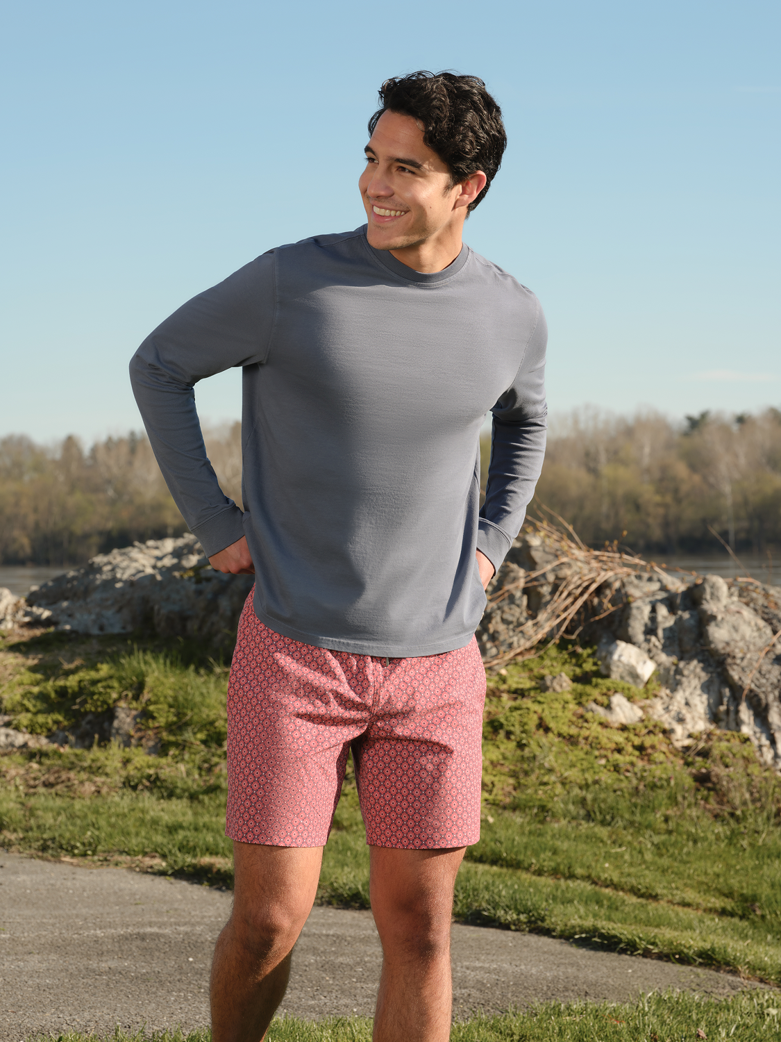 Man wearing a gray long sleeve graphic tee and red patterned shorts standing outdoors.