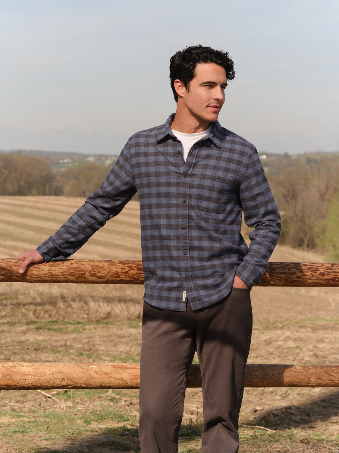 Man wearing a blue and gray checkered flannel shirt with long sleeves over a white undershirt.