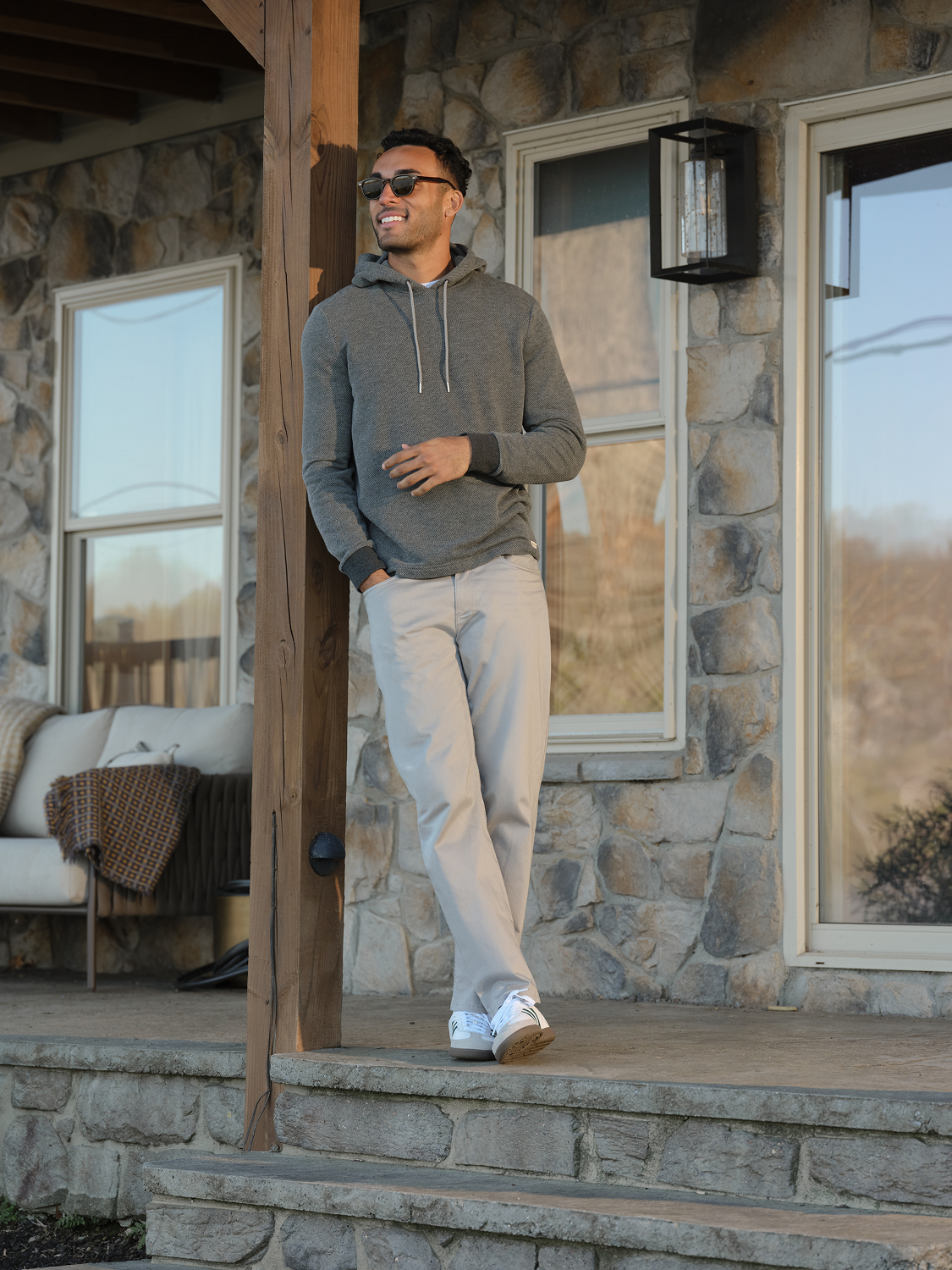 Man wearing a charcoal gray hoodie with drawstring paired with light beige pants and white sneakers.